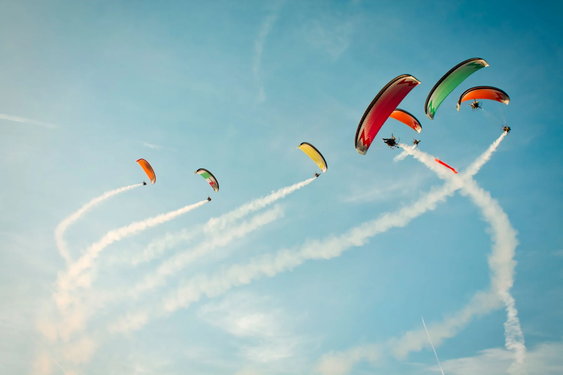 Farebné paraglidery na modrej oblohe